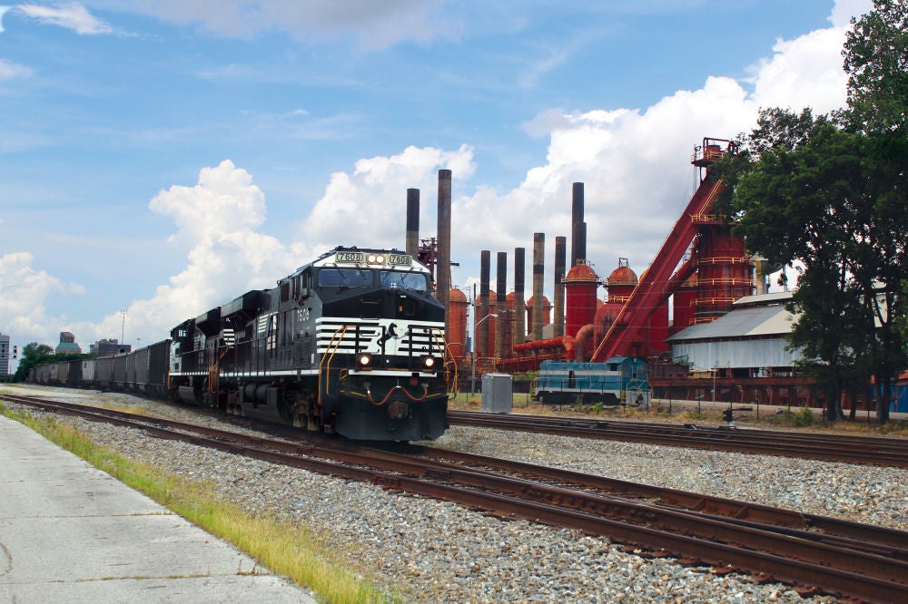 Norfolk Southern locomotives pull coal cars through a junction point on the mainline in Birmingham, Alabama, against the backdrop of the city’s historic Sloss Furnaces. NS operates 1,304 miles of track in Alabama.